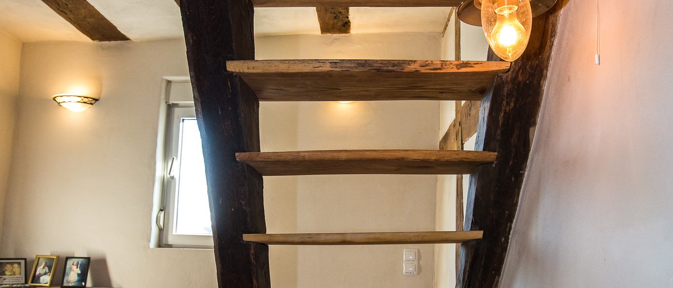 Treppenaufgang mit weiß gekalkten Wänden und historischem Holzgebälk